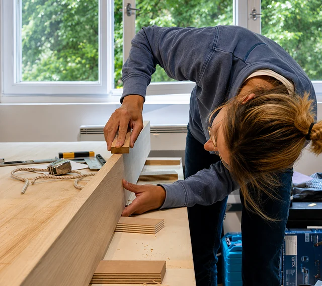 Alice Dubois ajuste une pièce en place sur un chantier, cale à poncer à la main.